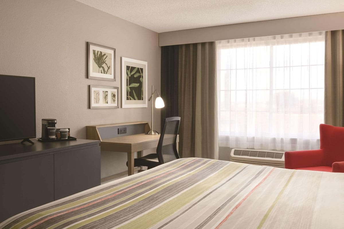 A hotel room with a bed, a desk, a chair, a TV, a lamp, and framed pictures on the wall.