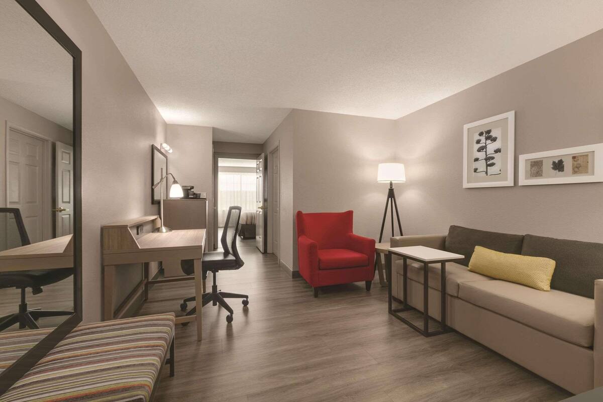 A modern living room with a sofa, armchair, desk, and lamp.