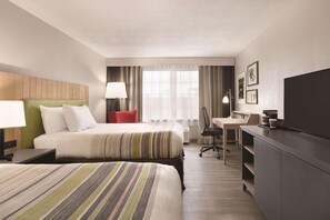 A hotel room with two beds, a desk, a chair, a TV, and a window with curtains.