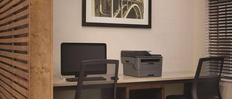 A workspace with a desk, two office chairs, a computer monitor, a printer, and a framed picture on the wall.