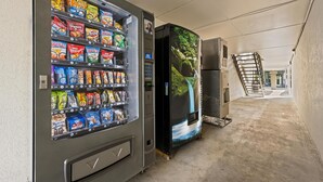 A vending machine stocked with snacks and a refrigerator with a waterfall mural. - Americas Best Value Inn Wilson (Wilson)
