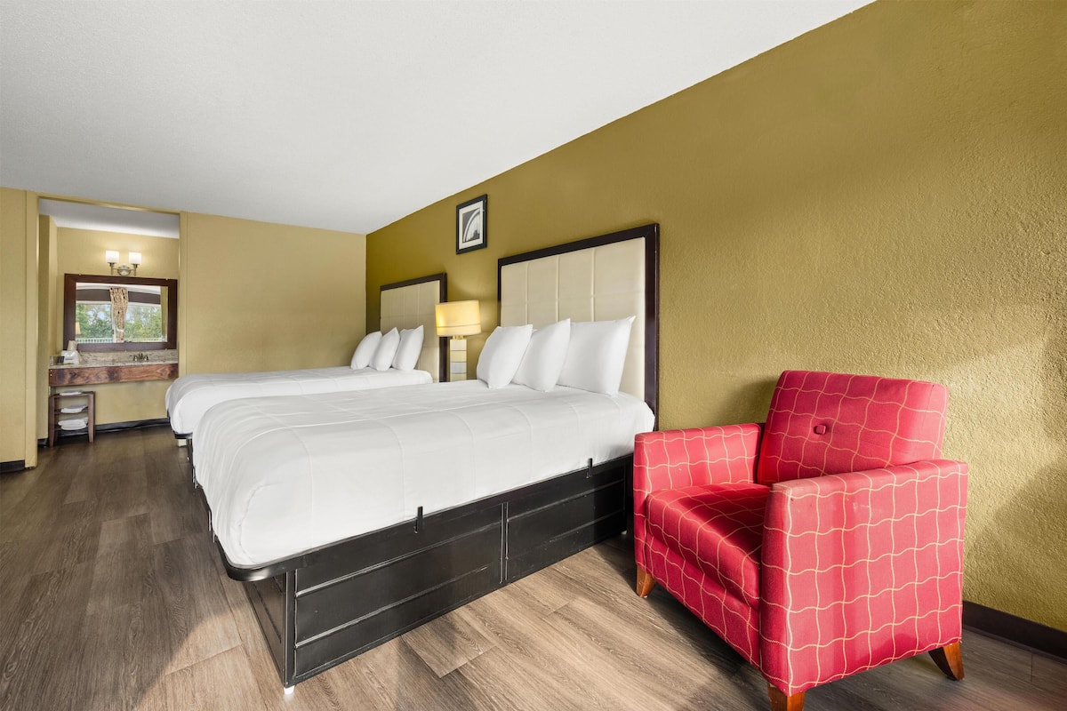 A hotel room with two beds, a red armchair, and a small desk with a lamp.