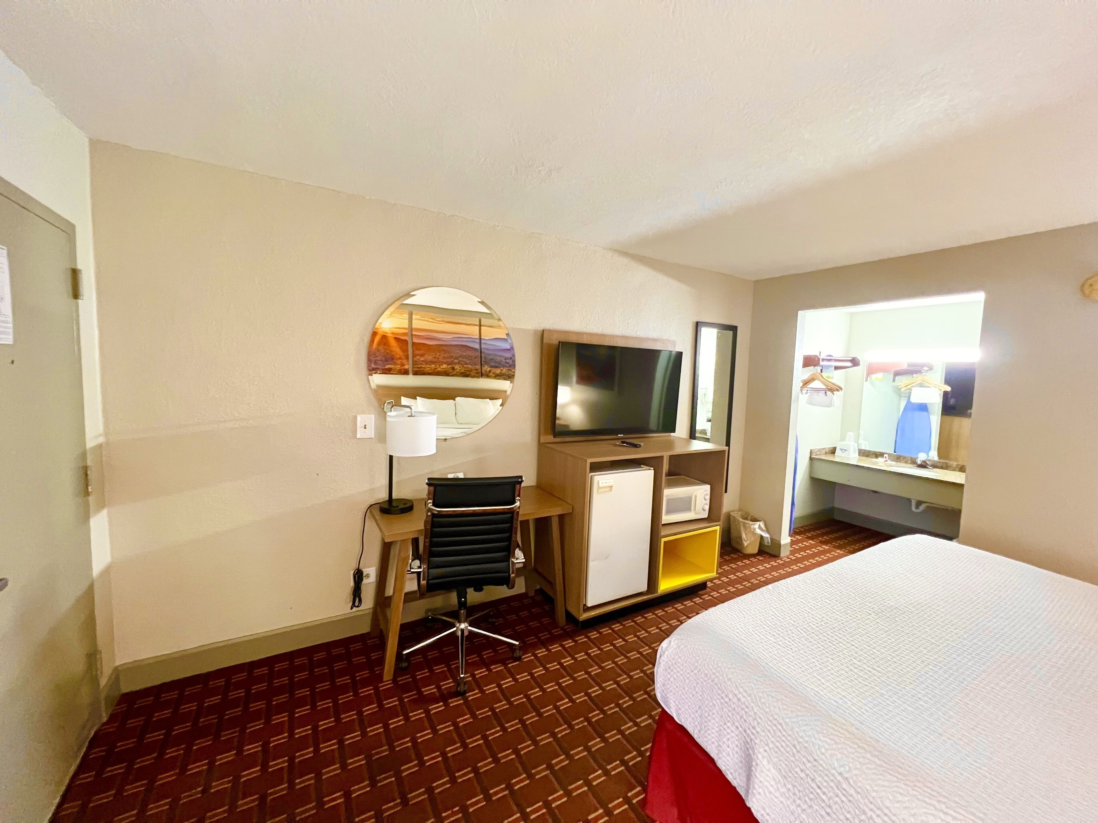 Ein Hotelzimmer mit einem Bett, einem Schreibtisch mit Stuhl, einem Fernseher, einem Spiegel, einer Mikrowelle und einem Fenster mit Blick.