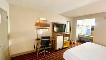 Habitación de hotel con cama, escritorio con silla, televisor, espejo, microondas y ventana con vistas.