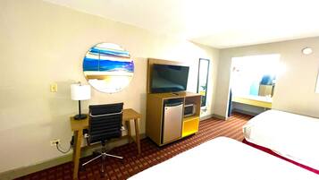 A hotel room with a bed, a desk with a chair, a television, a microwave, and a large mirror.