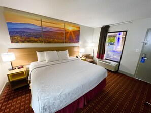 A hotel room with a large bed, a nightstand with a lamp, a chair, a window with curtains, and a wall-mounted painting. - Days Inn by Wyndham Athens (Athens)
