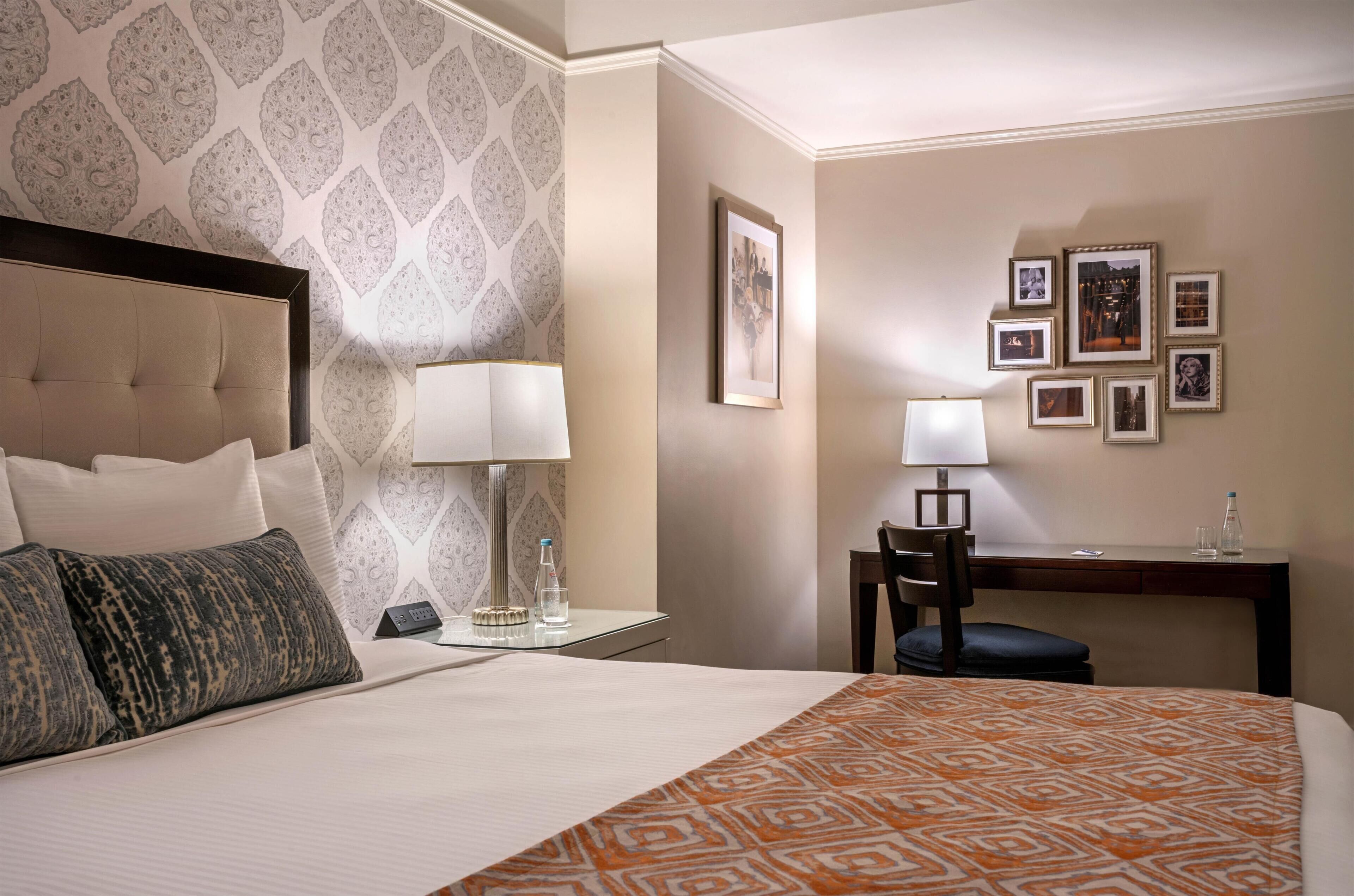 Een hotelkamer met een bed, een bureau, een stoel, een lamp en een wand met ingelijste foto's.
