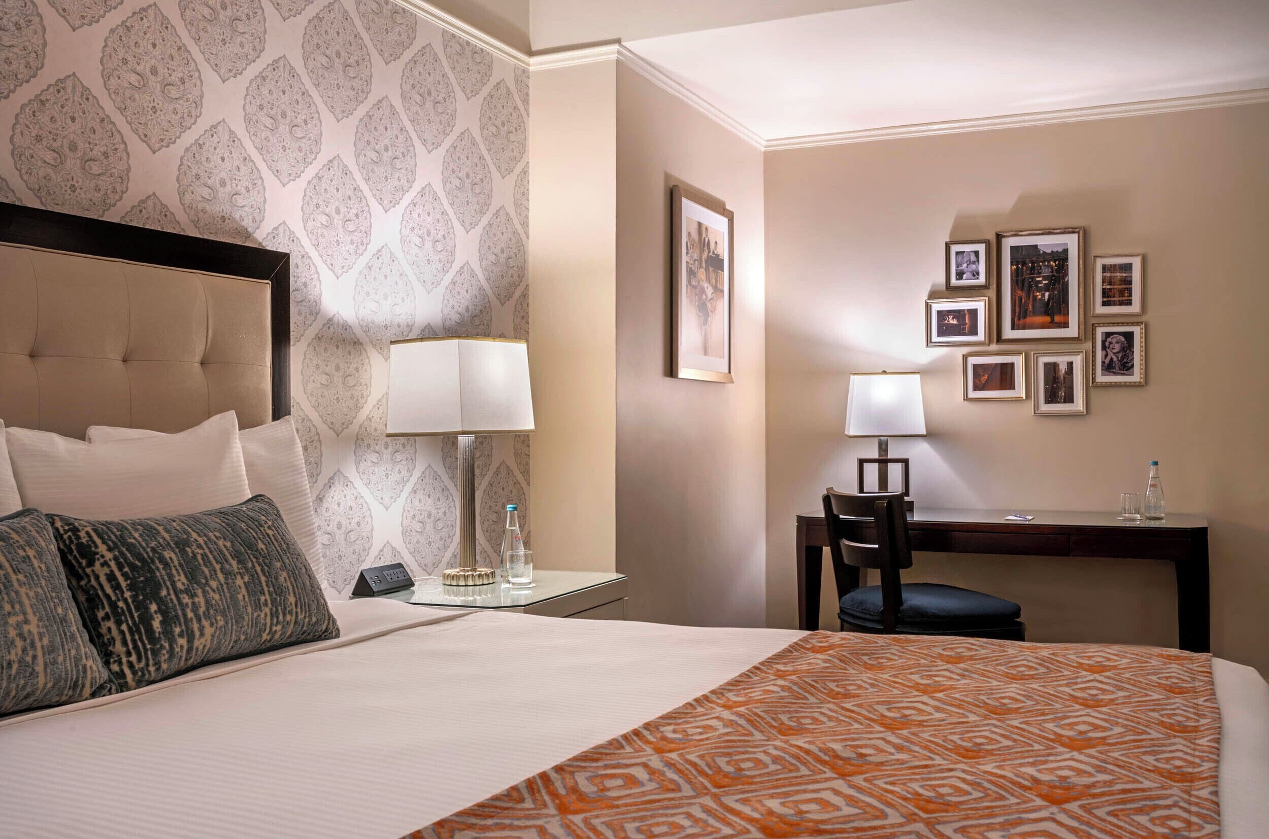 A hotel room with a bed, two bedside tables, a desk with a chair, and framed pictures on the wall.