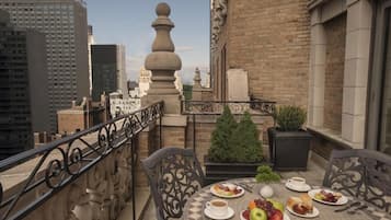 A rooftop terrace with a table set for breakfast, a small potted plant, and a view of the cityscape.