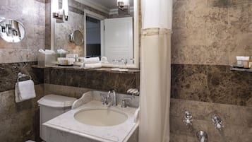 A bathroom with a marble sink, two faucets, a toilet, a mirror, and a shower curtain.