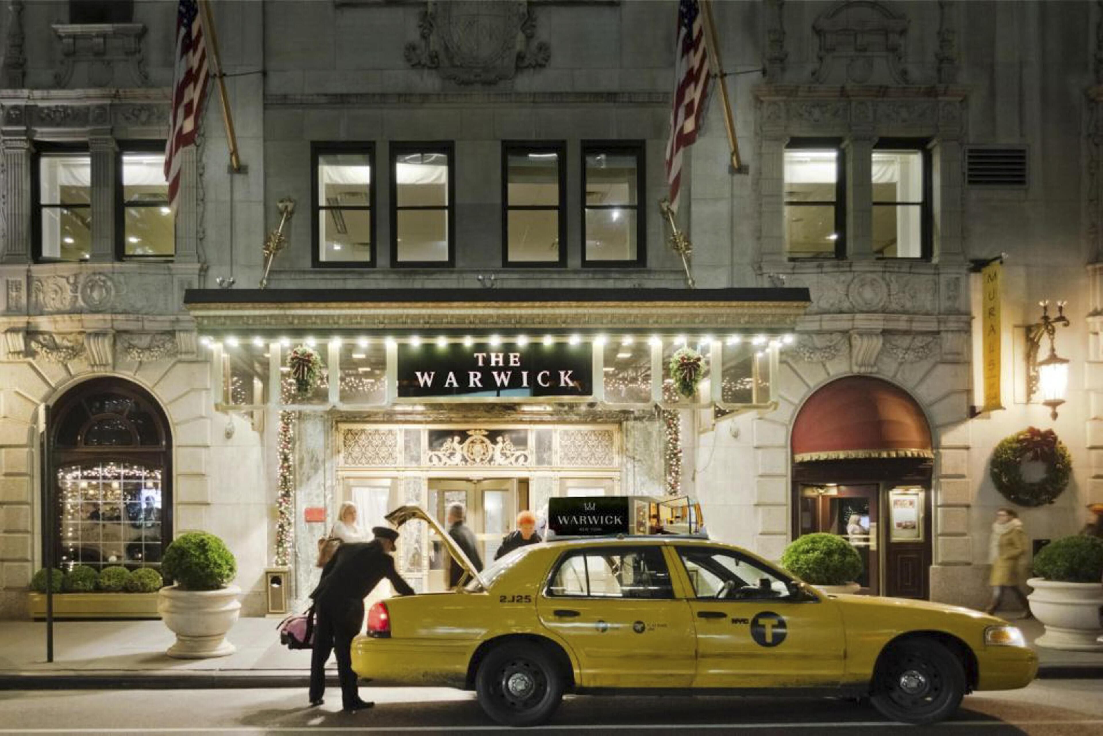 A classic building with a sign reading 'THE WARWICK' and a yellow taxi in front.