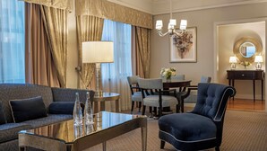 A hotel room with a sofa, armchair, dining table, and chairs. There is a lamp, a mirror, and a painting on the wall. - Warwick New York (New York)