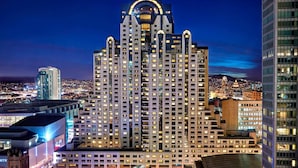 A high-rise building with a distinctive arched top and multiple floors, surrounded by other buildings and city lights at night.