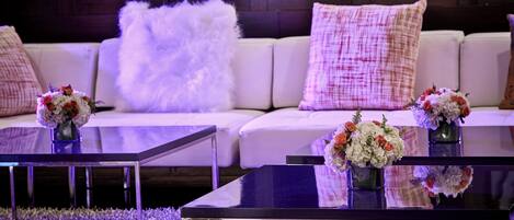 Una sala de estar moderna con un sofá blanco, almohadones mullidos y dos mesas de centro de vidrio con arreglos florales.