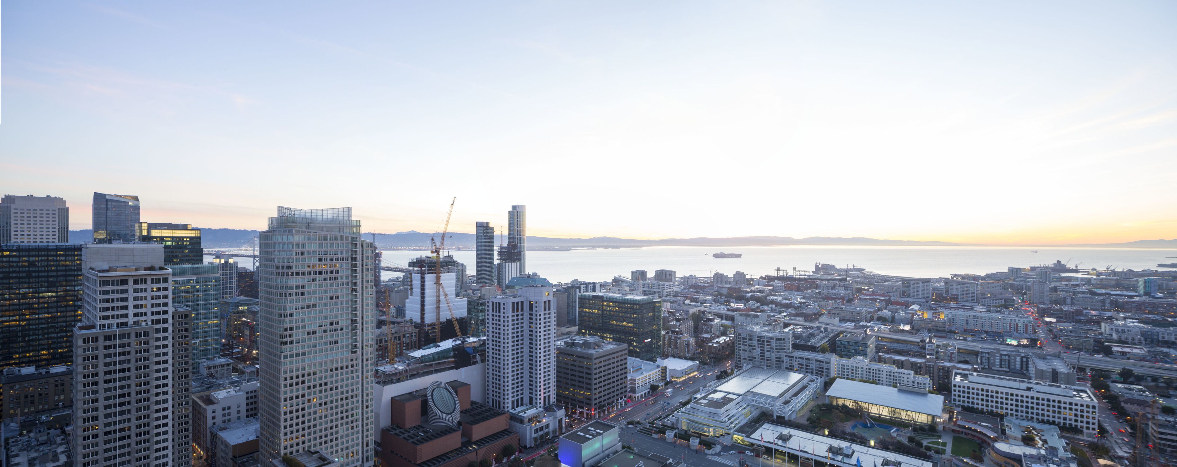 A cityscape with high-rise buildings, a bridge, and a body of water during sunset.