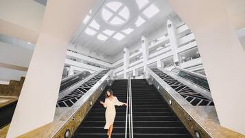 Une femme se tient sur un escalier dans un bâtiment moderne, doté d’un plafond haut et de lucarnes.