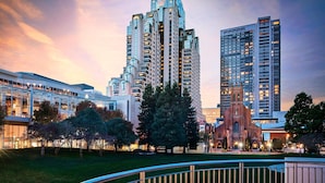 A modern high-rise building with a unique architectural design, surrounded by a well-maintained park and a historic church.