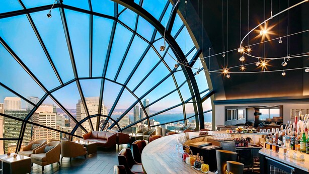 A modern bar area with a curved ceiling and large windows offering a city view.
