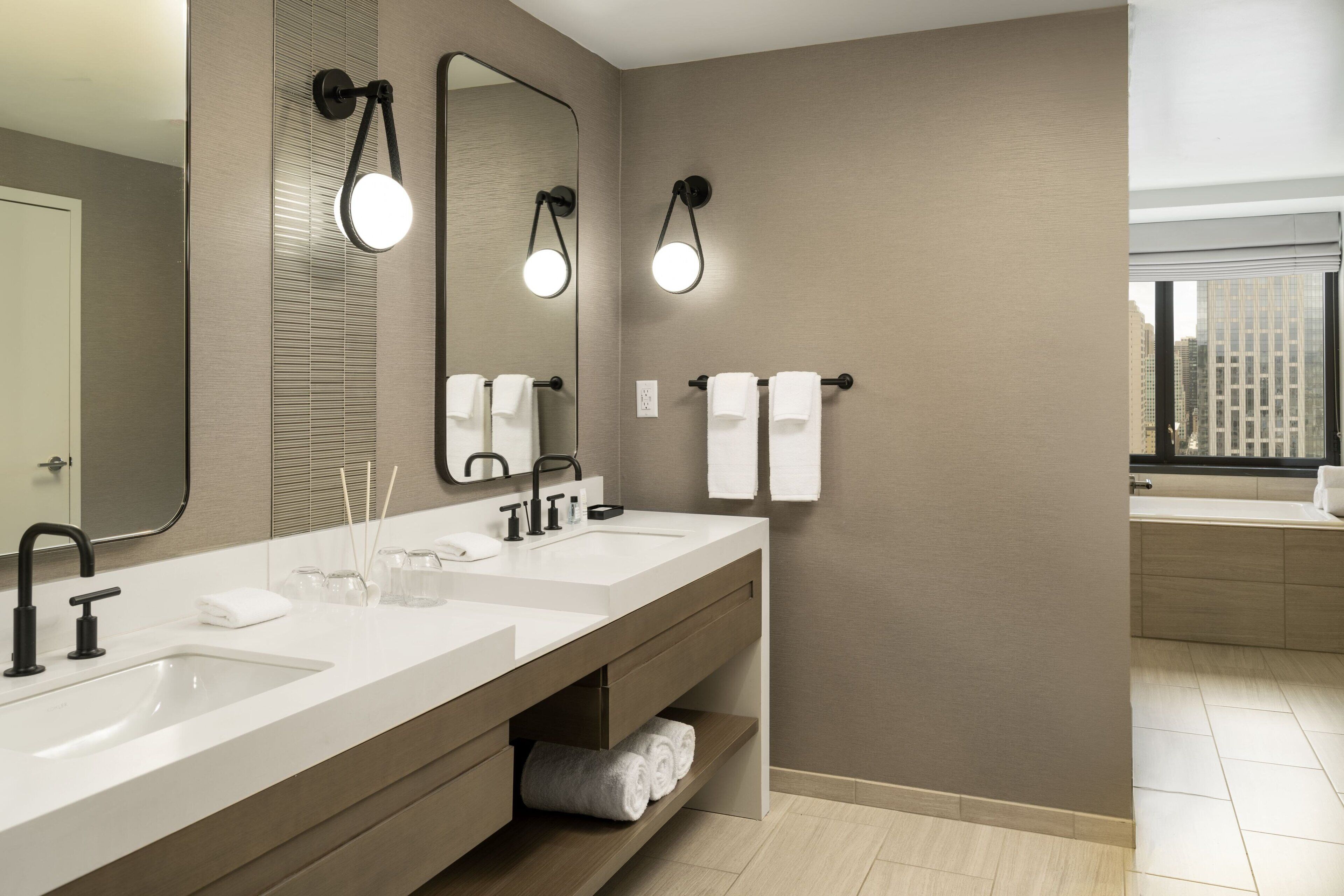 A modern bathroom with two sinks, a large mirror, and a window with a city view.