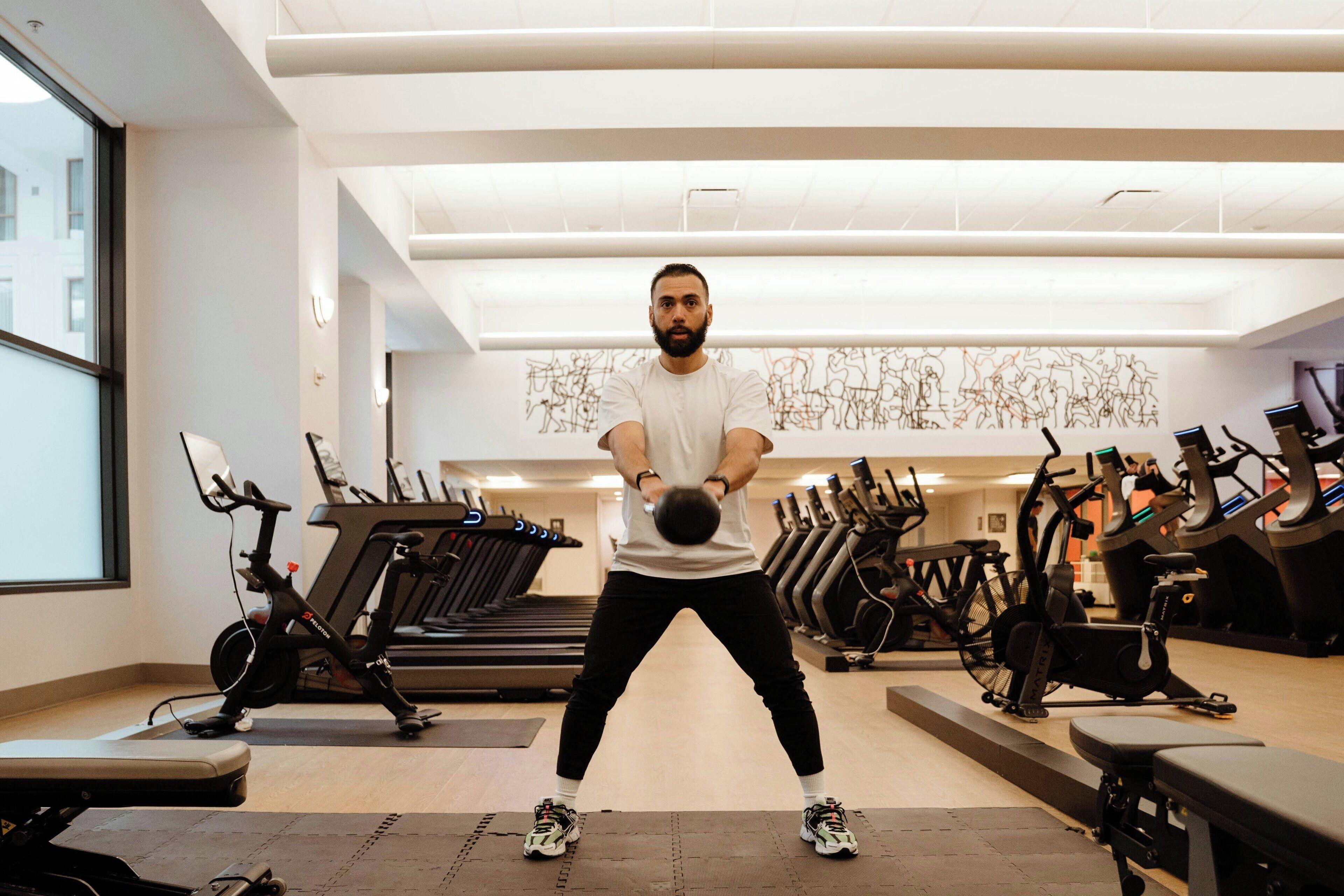 Ein Fitnessraum mit Laufbändern, Ergometer und einer Person, die eine Kettlebell-Übung macht.