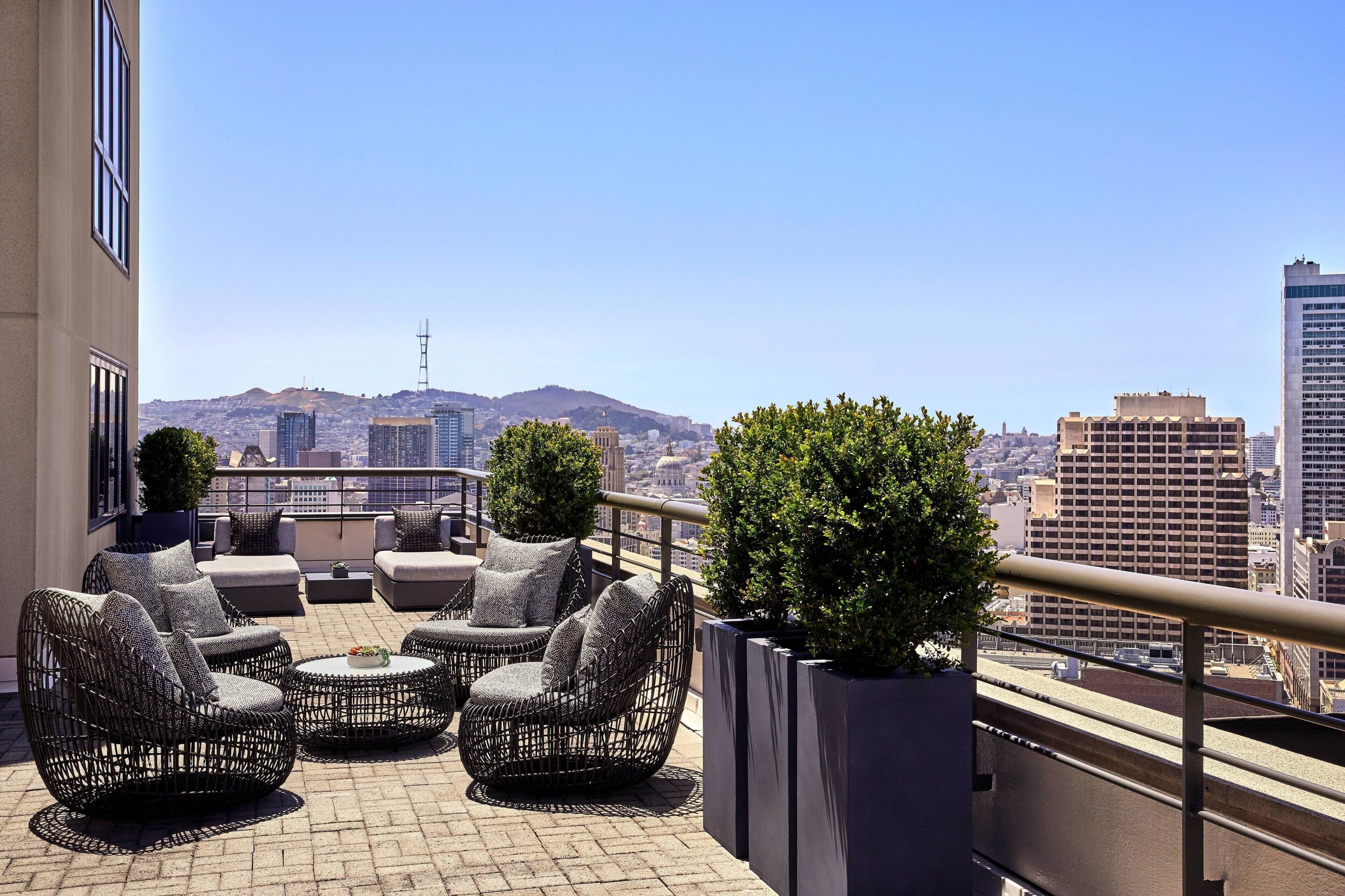 A rooftop terrace with wicker furniture and potted plants, offering a city view.