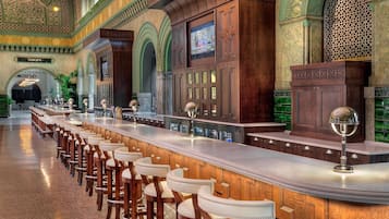 A long bar area with multiple stools and a high ceiling with intricate designs.