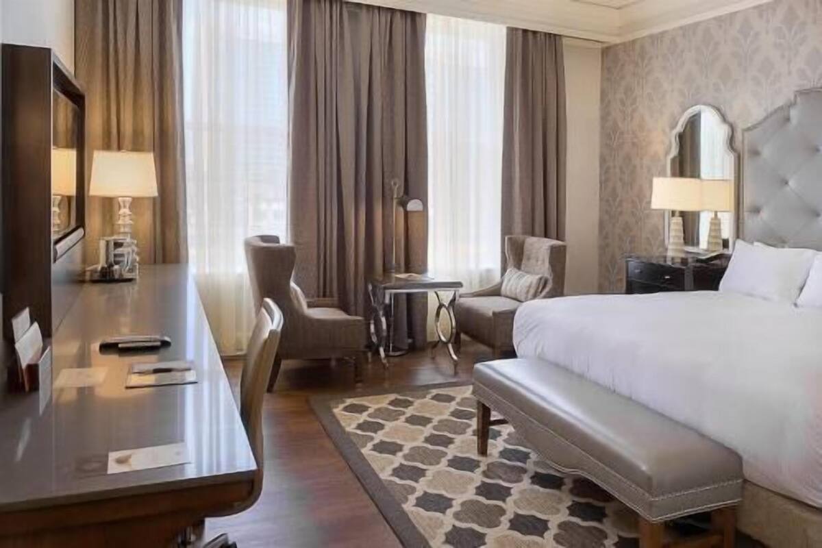 A hotel room with a bed, a desk, a chair, a small table, and a bench.