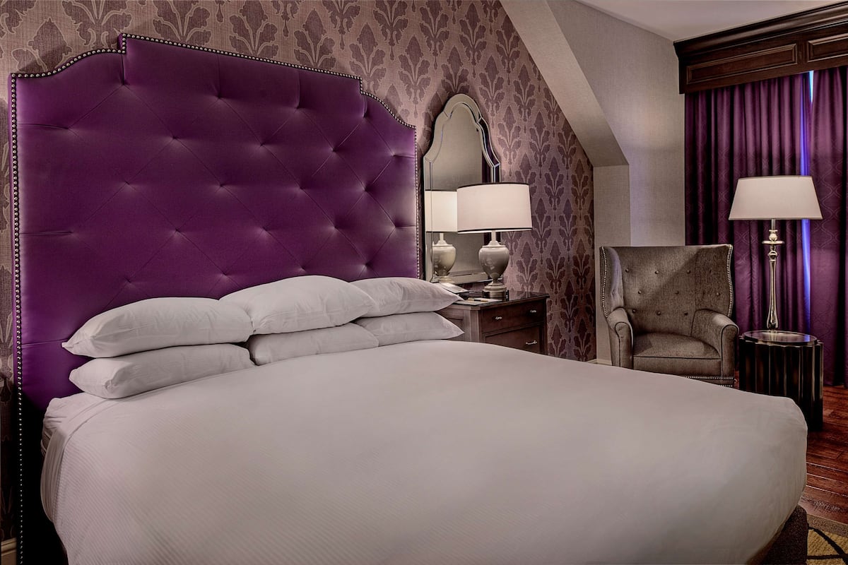 A large bed with a tufted headboard, a nightstand with a lamp, a chair, and a mirror.