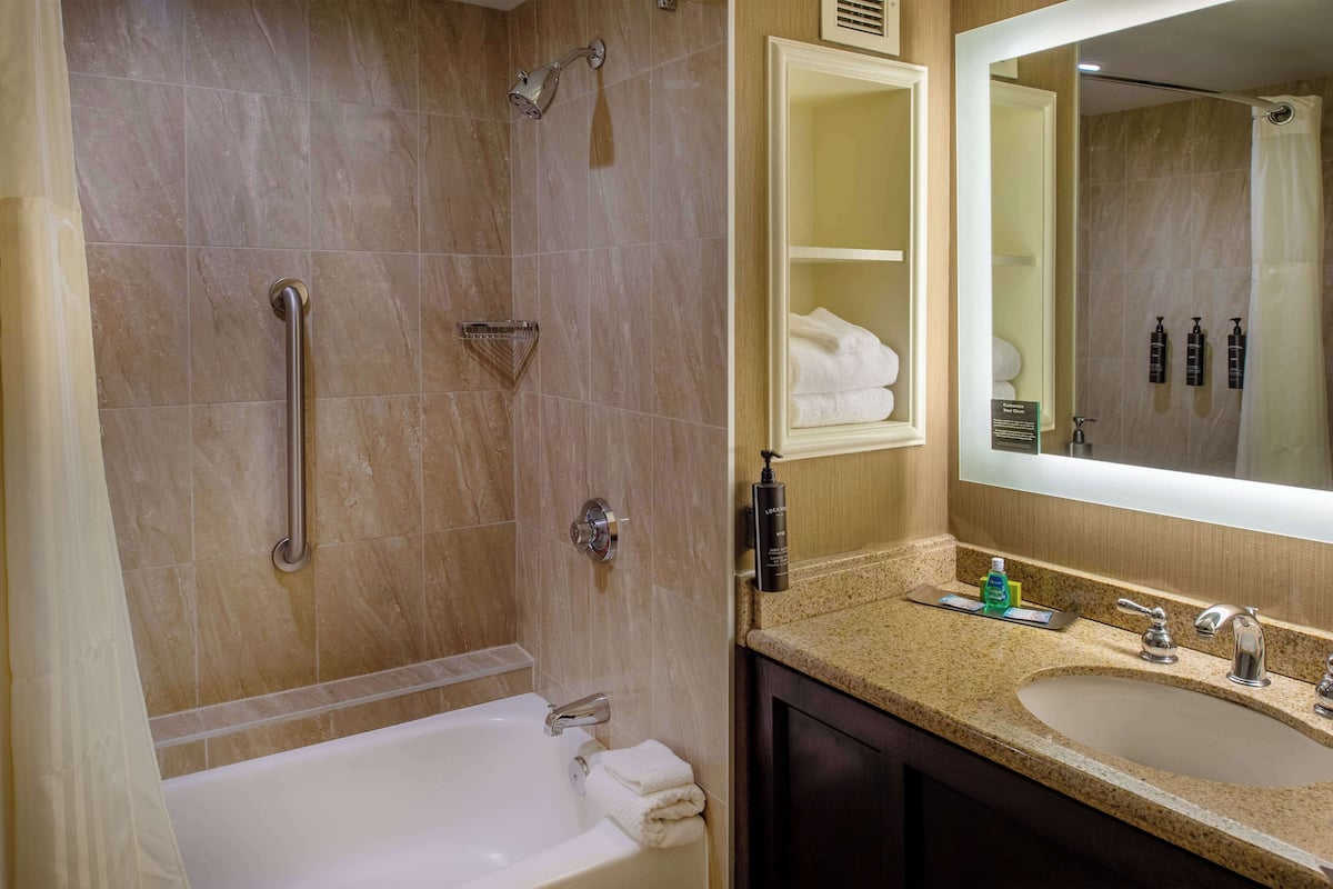 A bathroom with a bathtub, a shower with a grab bar, a sink with a mirror, and toiletries on the counter.