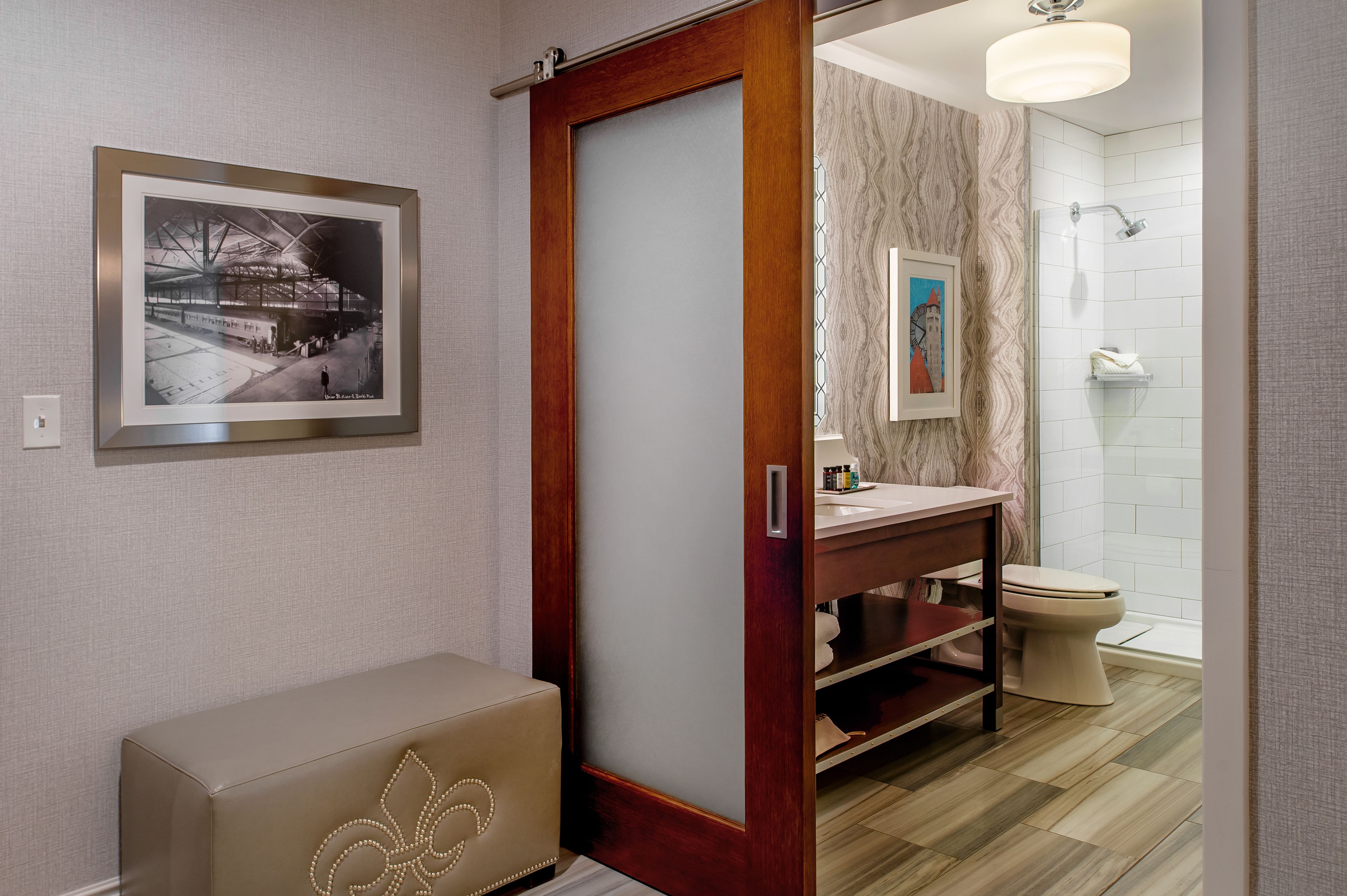 A modern bathroom with a wooden door, a framed picture on the wall, a bench, and a shower area.