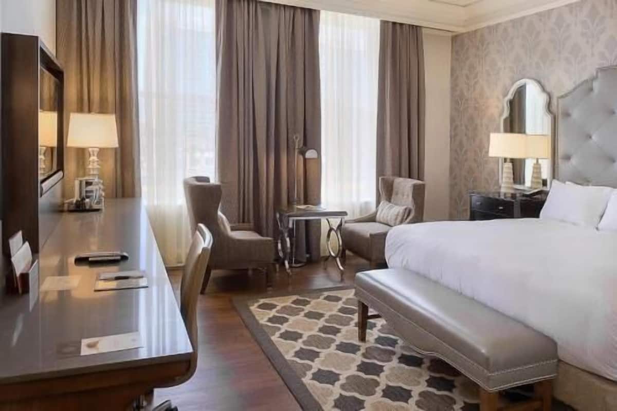 A hotel room with a bed, a desk, a chair, a small table, and a bench.