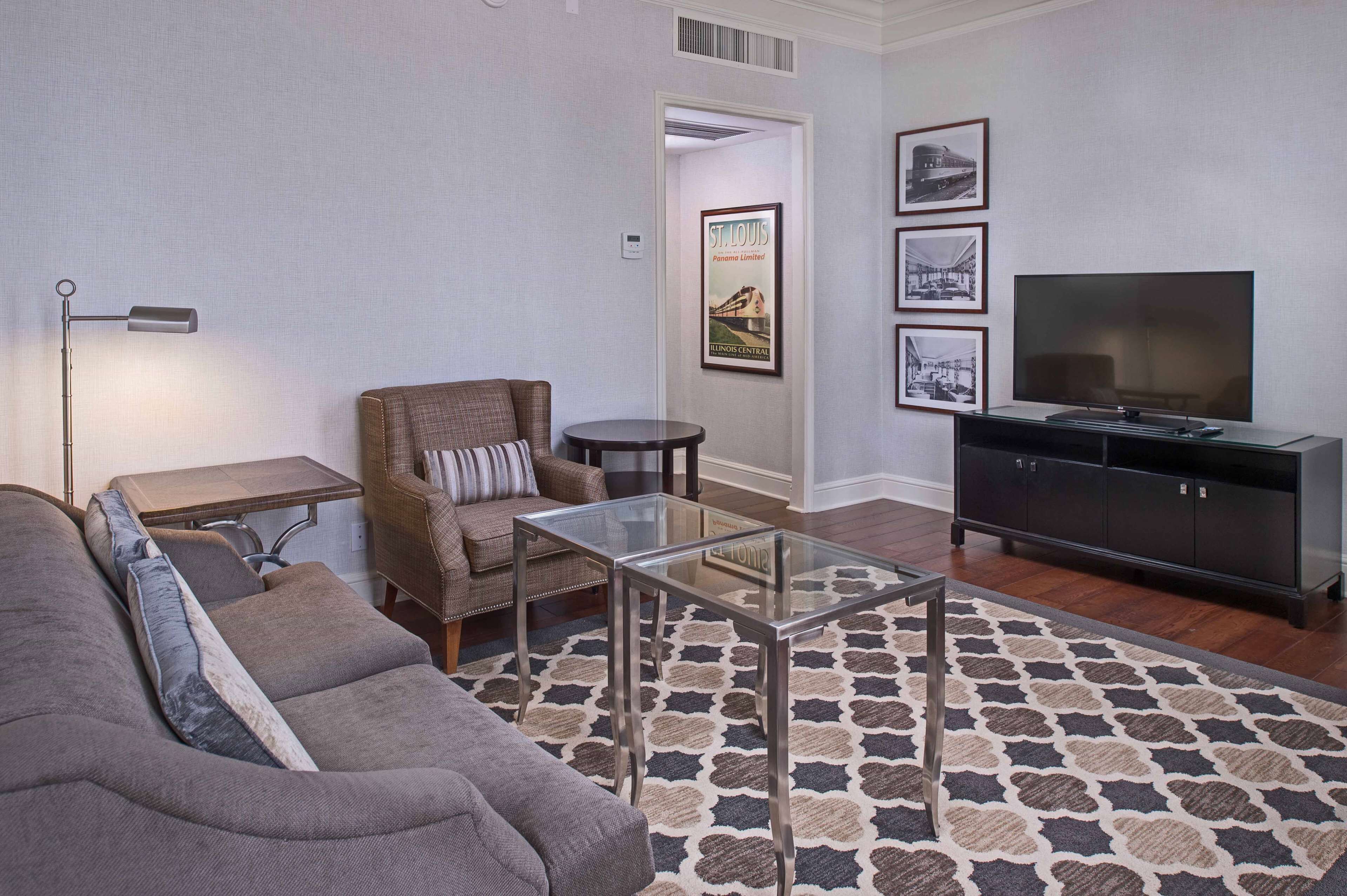A living room with a sofa, armchair, glass coffee table, TV, and a patterned rug.