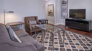 A living room with a sofa, armchair, glass coffee table, TV, and a patterned rug.
