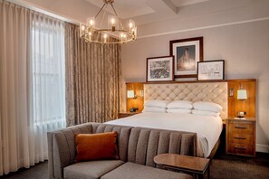 A hotel room with a large bed, a sofa, a chandelier, and framed pictures on the wall. - St. Louis Union Station Hotel, Curio Collection by Hilton (St. Louis)