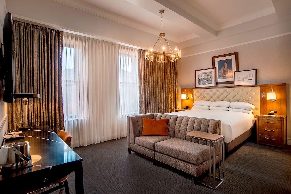 A hotel room with a large bed, a sofa, a desk, and a TV.