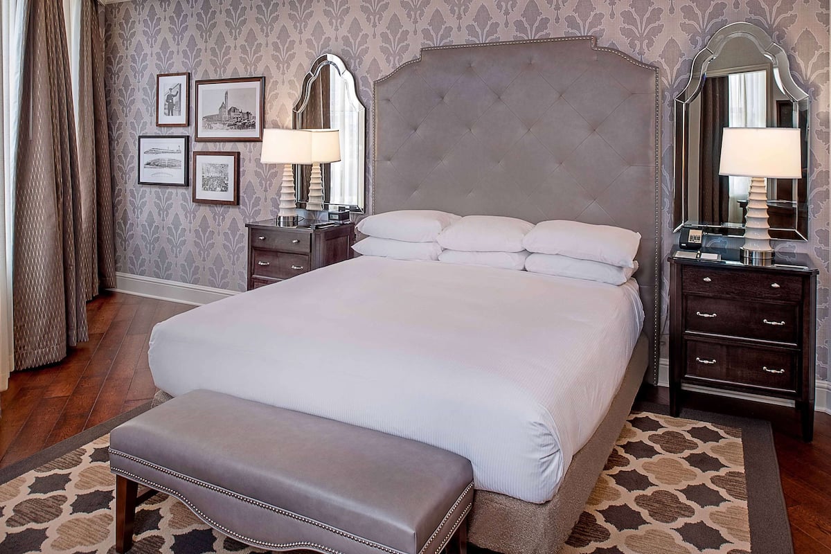 A neatly arranged hotel room with a large bed, a bedside table, a nightstand, a mirror, and a wall with framed pictures.