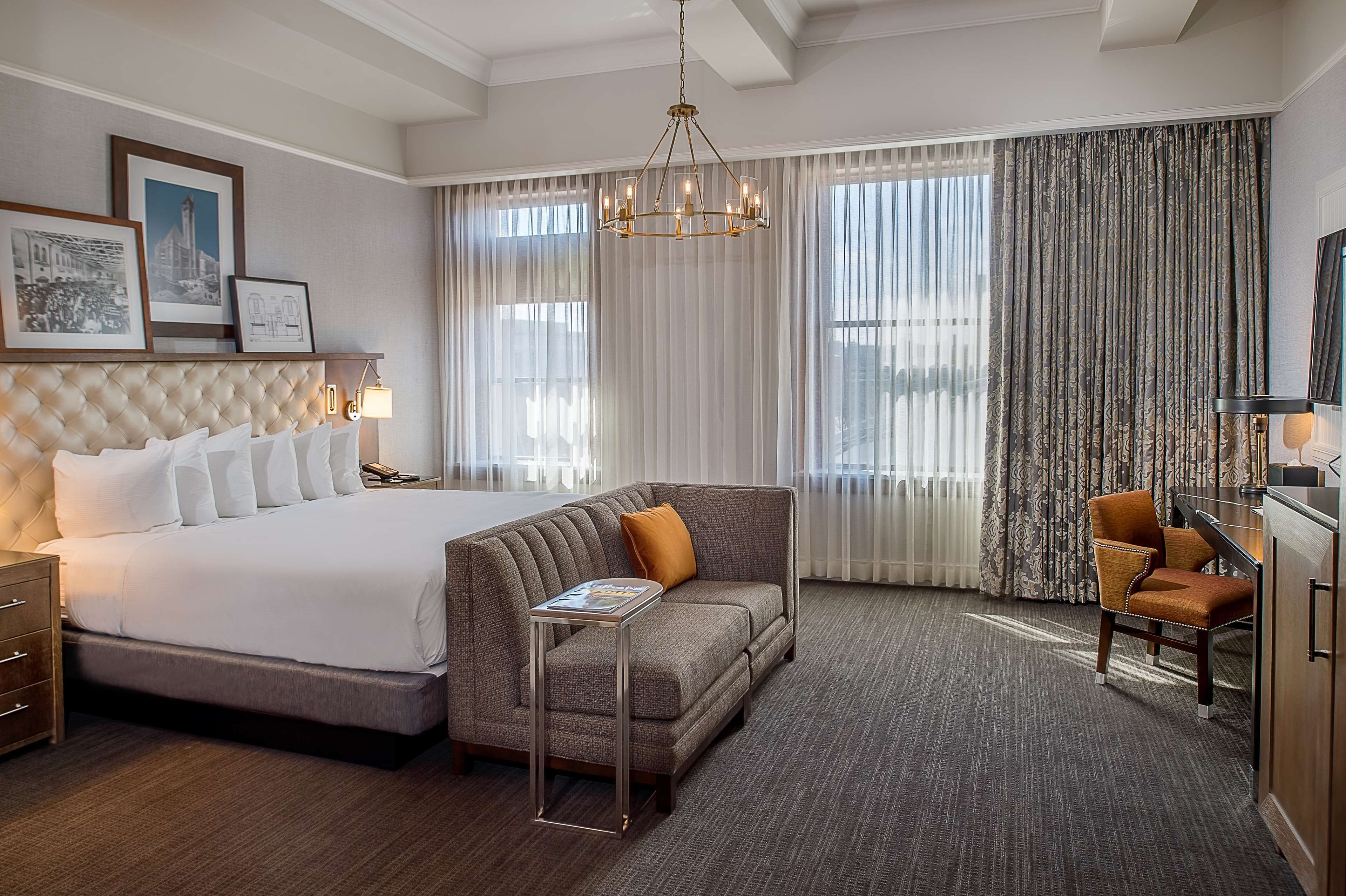 A hotel room with a large bed, a sofa, a desk, and a chandelier.