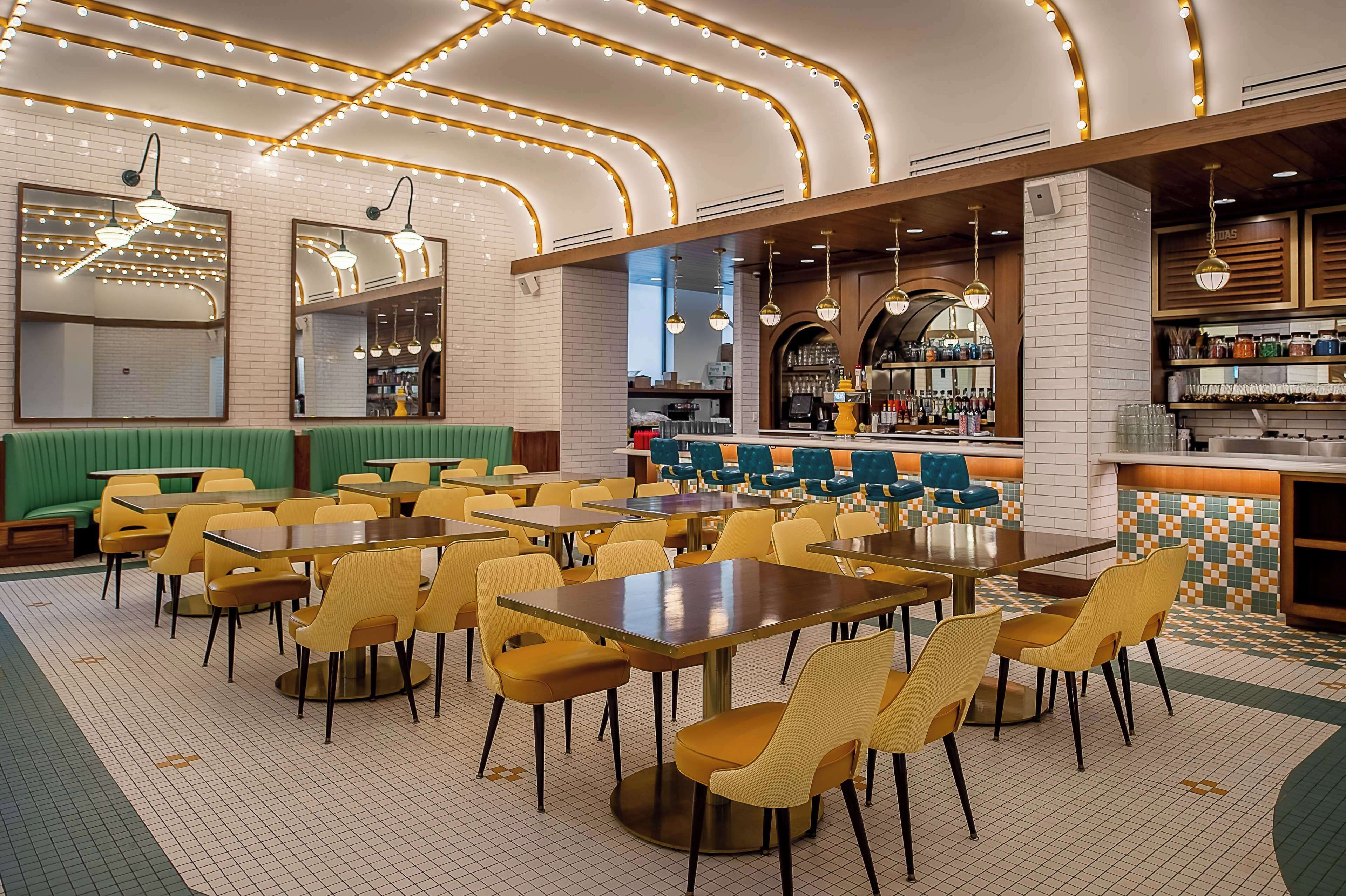 A restaurant with multiple tables and chairs, a bar area, and a seating section with green booths.