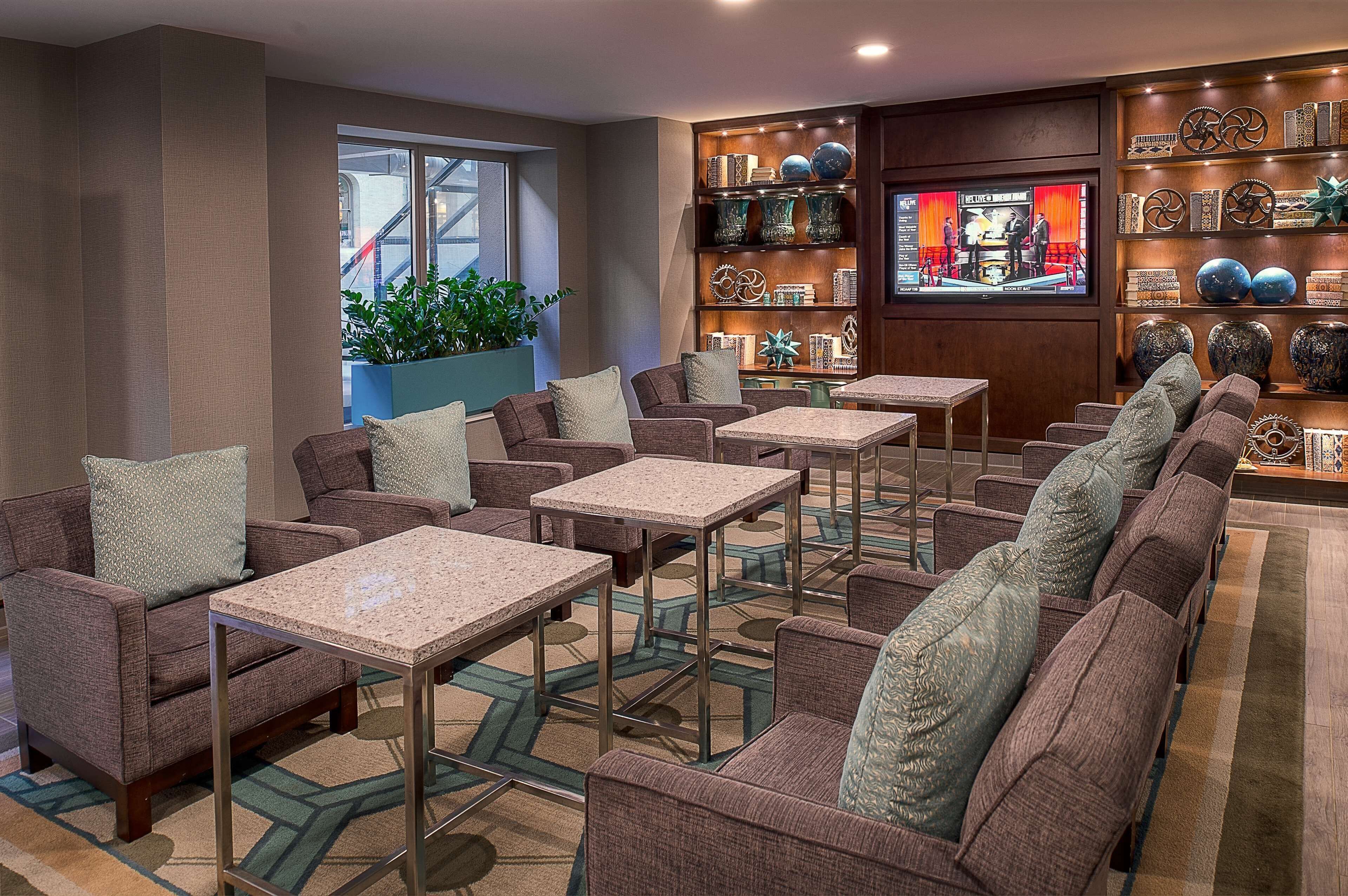 A hotel lobby with multiple seating areas, a television screen, and a decorative wall with vases and sculptures.