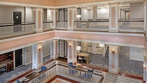 Un vestíbulo de hotel de varios niveles con una imponente escalera, una recepción y un área de descanso.