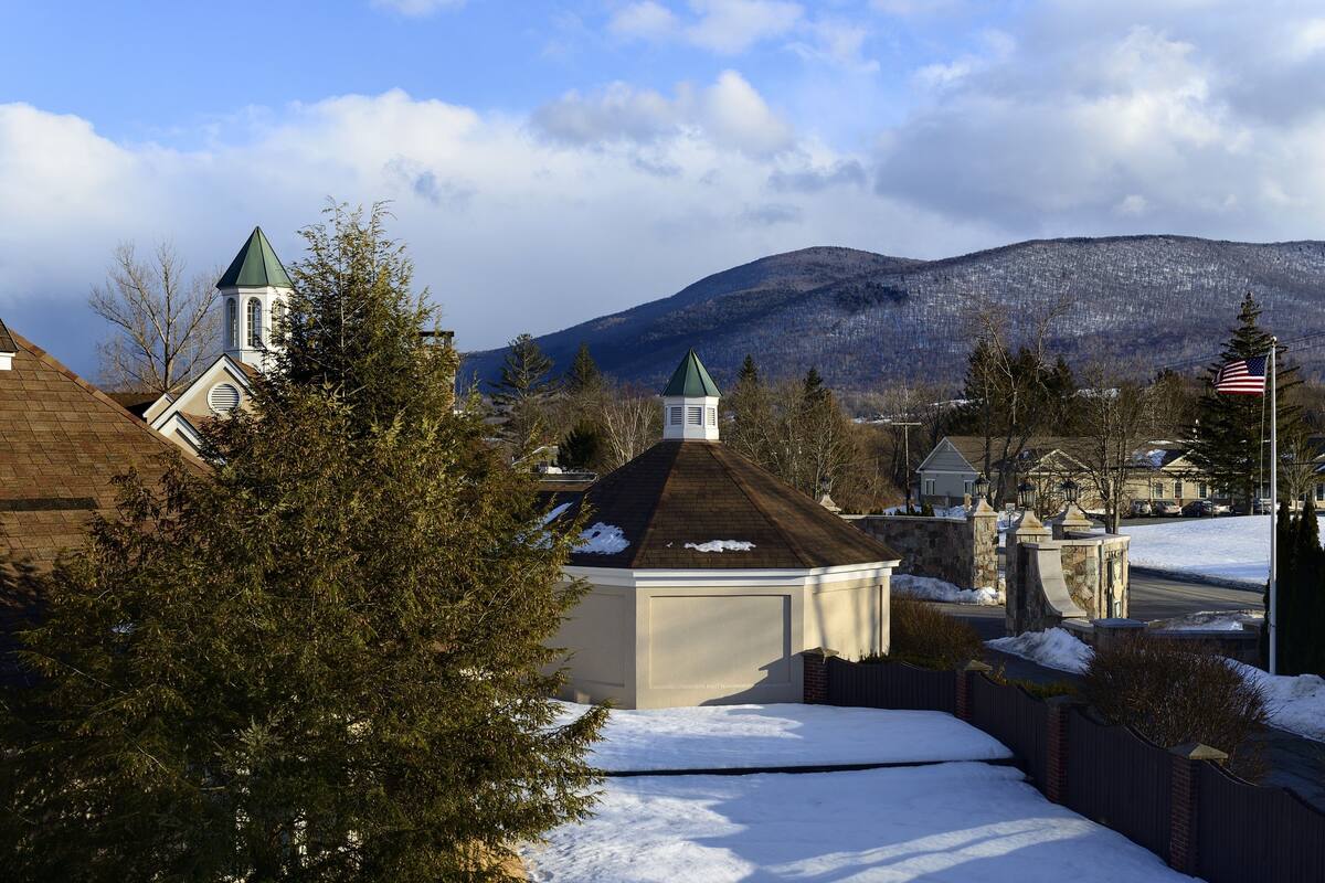A residential area with snow-covered ground, a church with a green steeple, and a mountain in the background.