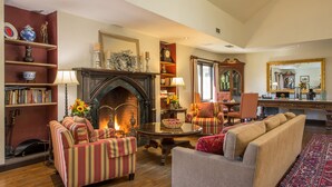 A cozy living room with a fireplace, striped armchairs, a sofa, and a bookshelf filled with books. - The Orchards Hotel (Williamstown)