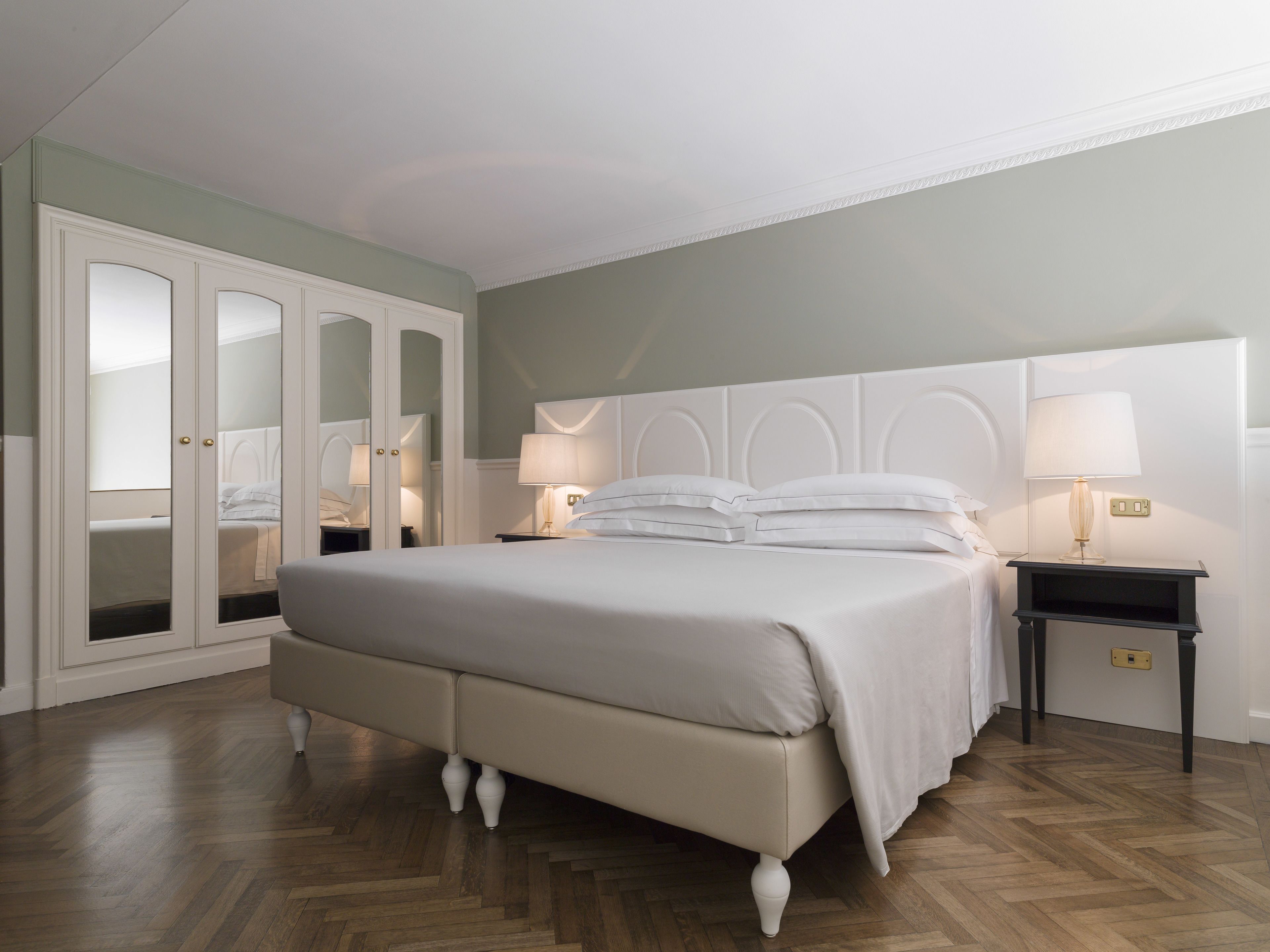 A bedroom with a bed, nightstands, a mirror, and a wardrobe.