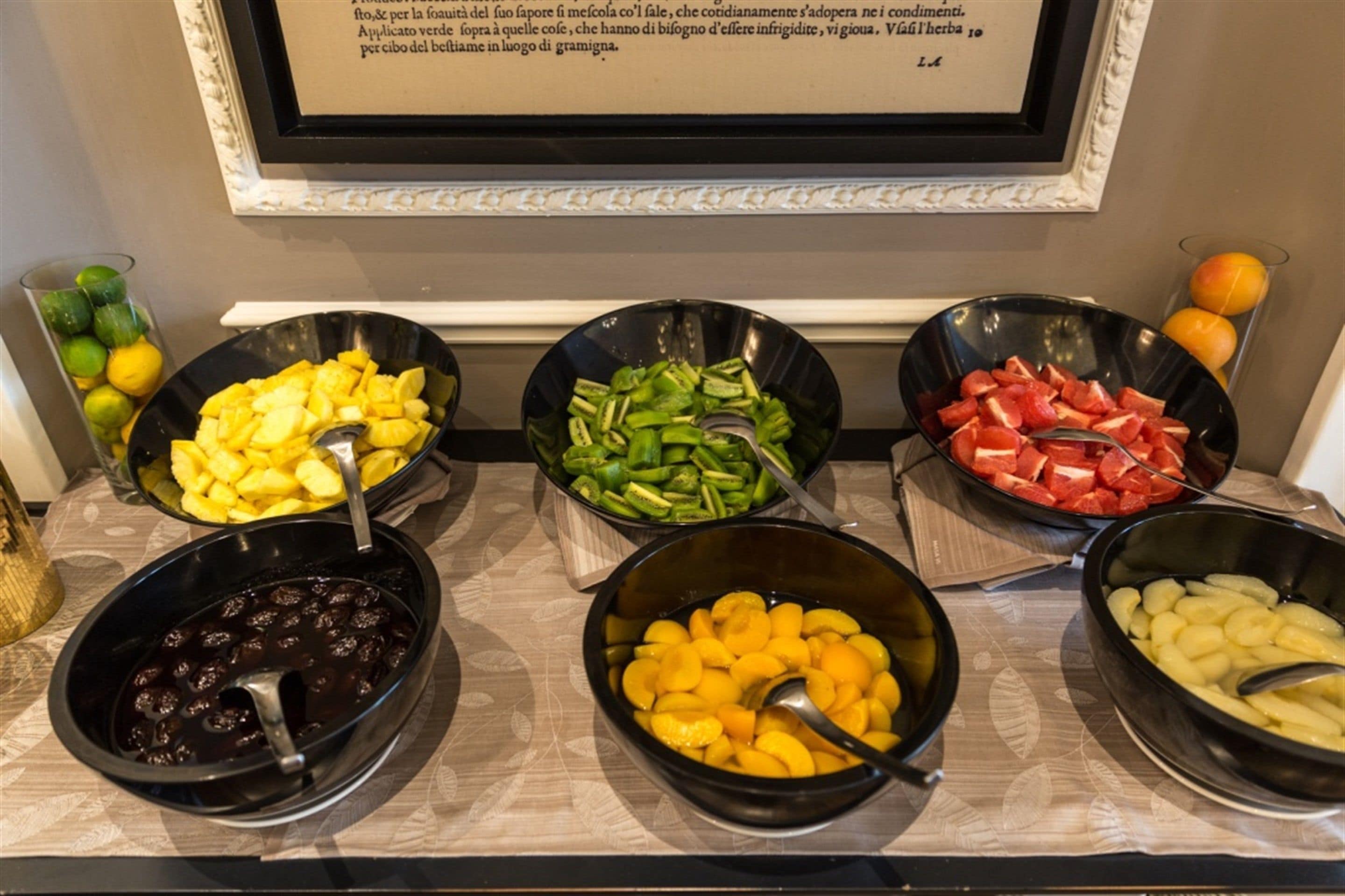 A buffet with various fruits and vegetables in bowls, a framed menu above, and a decorative wall.