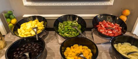 A buffet with various fruits and vegetables in bowls, a framed menu above, and a decorative wall.