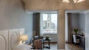 A hotel room with a bed, a desk, a chair, a table with flowers, and a view of a church through a window. - Plaza Hotel Lucchesi (Florence)