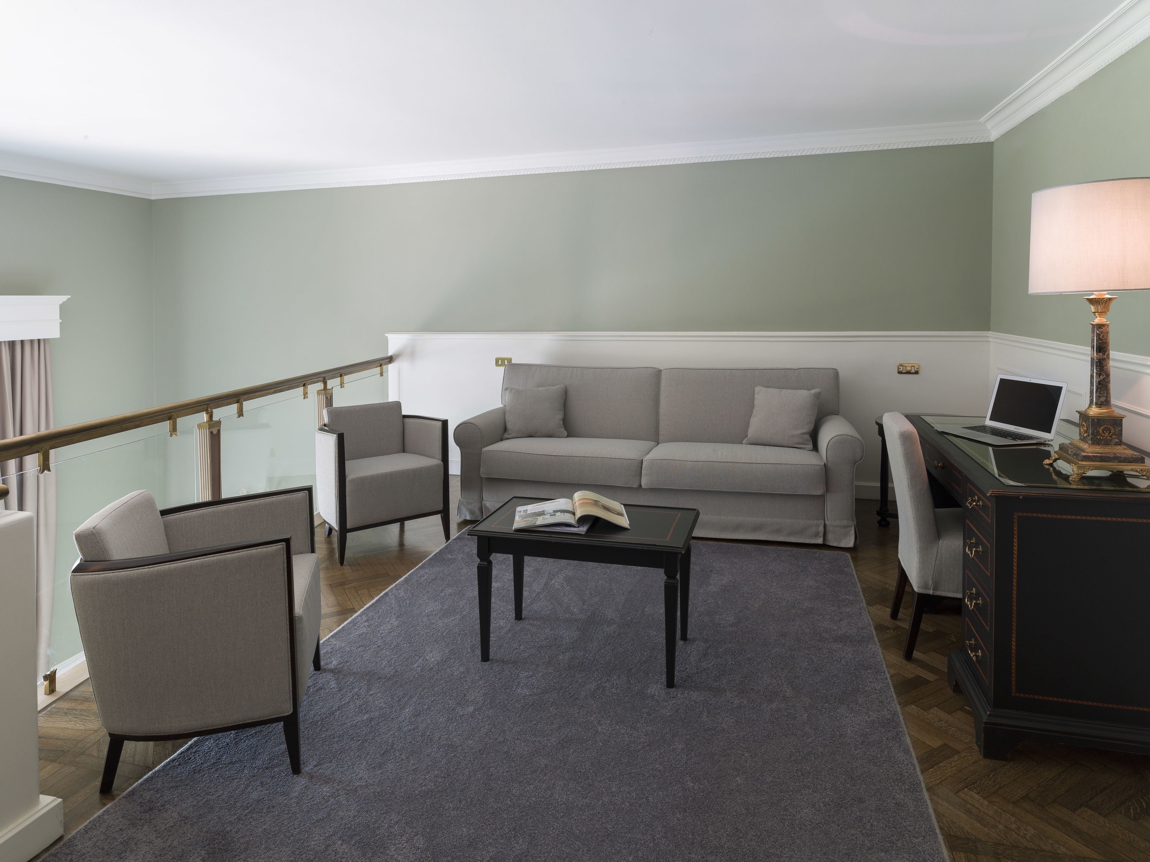 A living room with a sofa, armchair, coffee table, and a desk with a lamp.