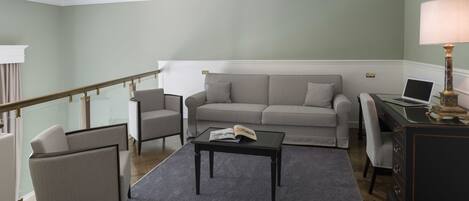 A living room with a sofa, armchair, coffee table, and a desk with a lamp.