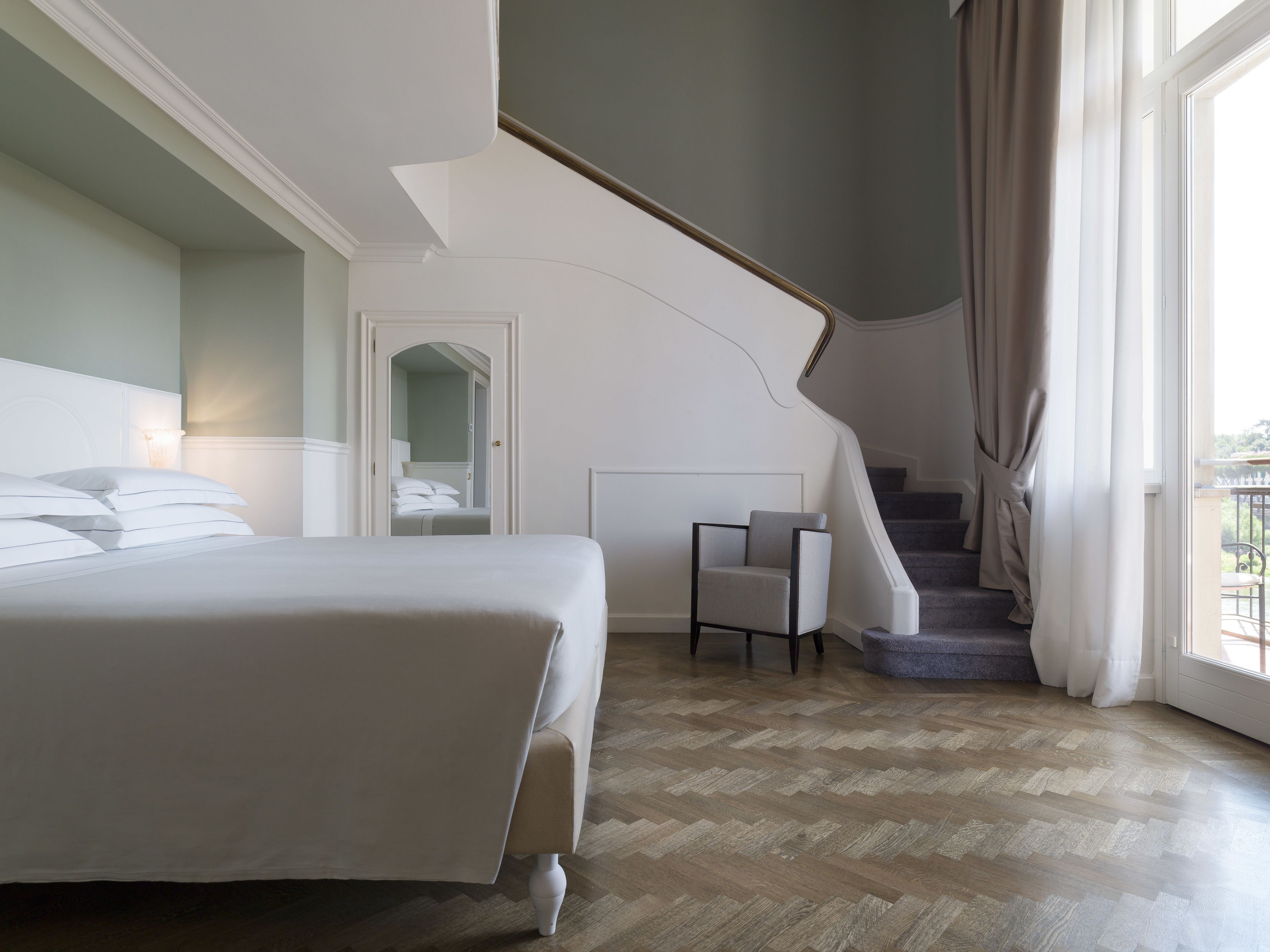 Una camera da letto con un letto, una sedia, una scala e una porta che dà su un'altra stanza.