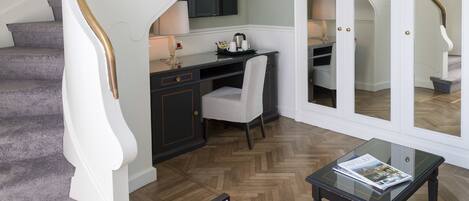 Un vaste espace de vie doté d’un parquet en bois à motifs en chevrons, d’un escalier également à motifs en chevrons, et d’un coin salon comprenant deux fauteuils et une table basse.
